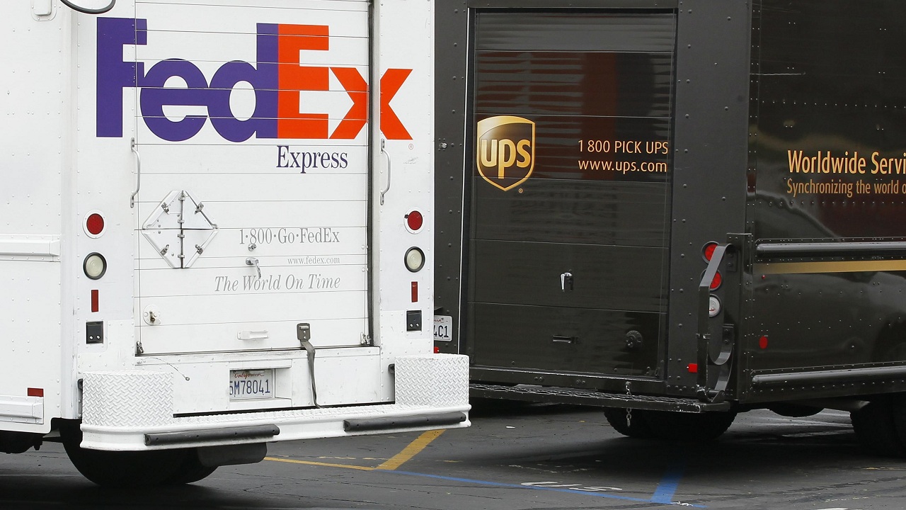 A FedEx truck is parked next to a UPS truck as both drivers make